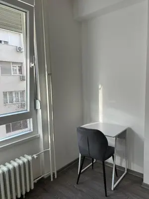 a table and a chair in a room with a window at Tesla Lux Apartman in Belgrade