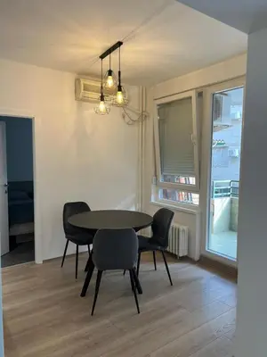 a dining room with a table and chairs and a window at Tesla Lux Apartman in Belgrade