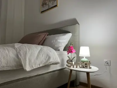 a bed with white sheets and a table with a flower on it at Gold Star Apartman in Ruma