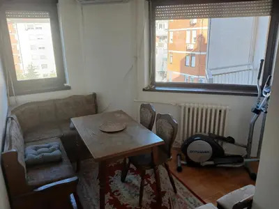 a table and chairs in a room with two windows at Apartman86 in Beograd