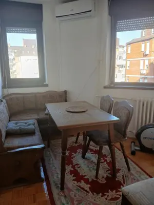 a living room with a table and a couch and two windows at Apartman86 in Beograd