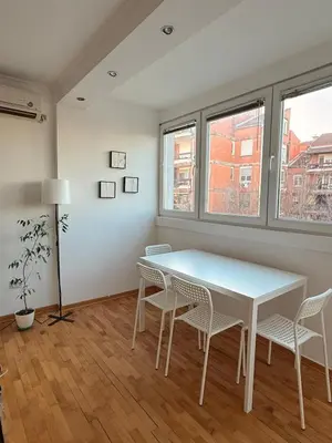 a white table and chairs in a room with windows at Light & Cozy Flat Banovo Brdo in Belgrade