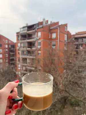 a person holding a cup of coffee with a building in the background at Light & Cozy Flat Banovo Brdo in Belgrade