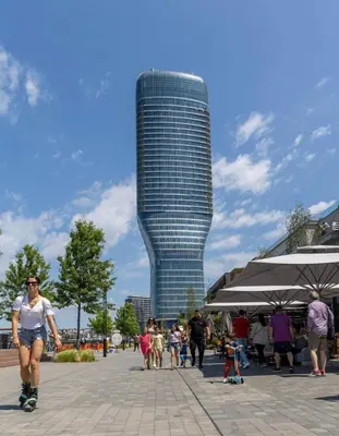 a woman is rollerblading in front of a tall building at 1 Beograd na Vodi Belgrade Waterfront posaljite poruku radi info o nacinu ulaska i preuzimanje kljuca in Belgrade