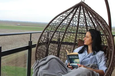 a woman sitting in a hammock reading a book at Apartman Nina Banovci in Novi Banovci