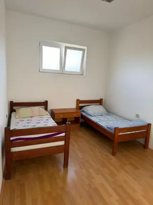 two beds in a room with wooden floors and a window at Pecinci Hostel in Pećinci