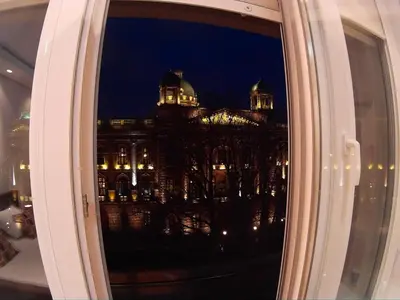 a window with a view of a building at night at Balkan-inn Parlament apartment in Belgrade