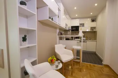 a living room with white chairs and a kitchen at Lux Life Apartment in Belgrade