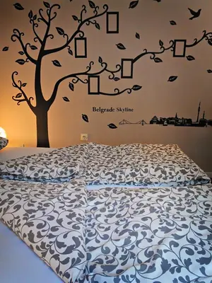 a bedroom with a bed with a tree on the wall at Banshill Apartment in Belgrade
