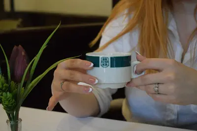 a woman sitting at a table holding a coffee mug at Queen's Astoria Design Hotel in Belgrade