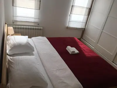 a bedroom with a bed with two white sheets and two windows at Apartment Triton in Belgrade