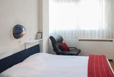 a bedroom with a bed and a chair and a window at Apartment La Bombonera in Belgrade