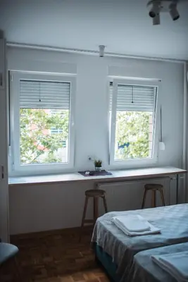 two windows in a bedroom with a bed and two stools at Arena East Apartment in Belgrade