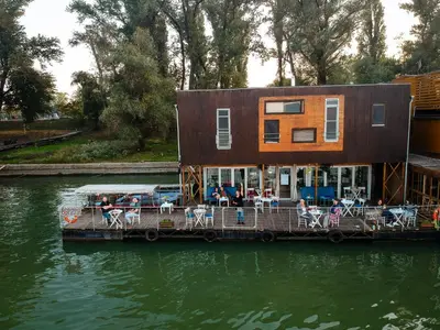 a house on a dock with tables and chairs on the water at ArkaBarka Floating Hostel in Belgrade