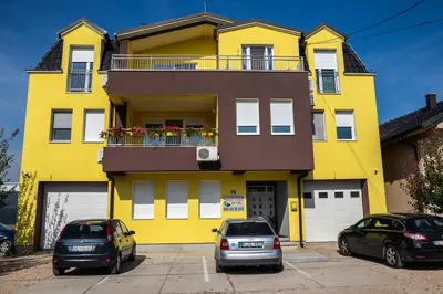 two cars parked in front of a yellow building at Kalanj Apartmani I Sobe in Belgrade