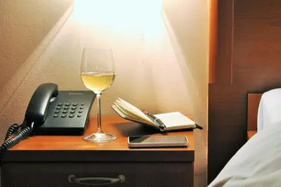 a glass of wine and a phone on a nightstand with a glass of white at Hotel Rex in Belgrade