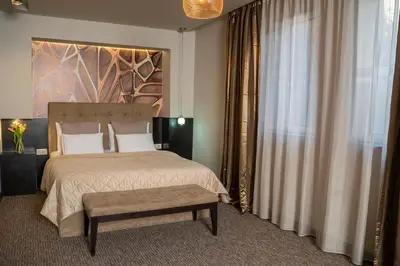 a bedroom with a large bed with a bench next to a window at Akacija Luxury Suites- Zemunski kej in Belgrade