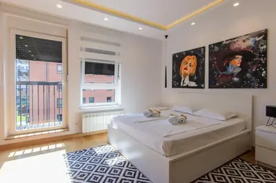a white bedroom with a bed and two windows at Sava Smart Apartment in Belgrade