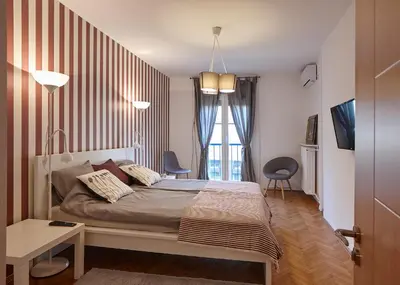 a bedroom with a bed with two chairs and a window at Take 5 in Belgrade