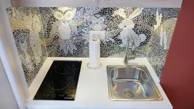 a sink in a small kitchen with a mosaic wall at Apartman Mia in Belgrade