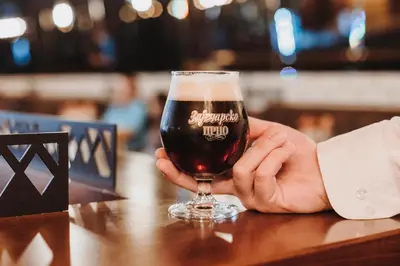 a person holding a glass of beer on a table at Avenia Restaurant & Apartments in Ruma