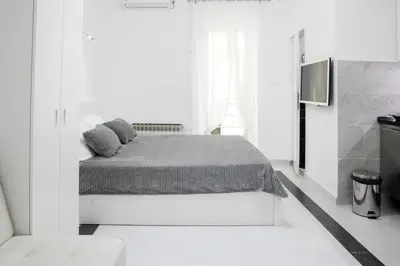 a white bedroom with a bed and a tv at Natalie's Studio in Belgrade