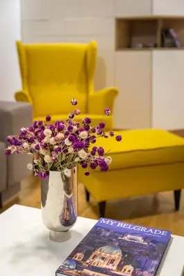 a vase with purple flowers on a table next to a yellow chair at Delights Apartment Belgrade in Belgrade