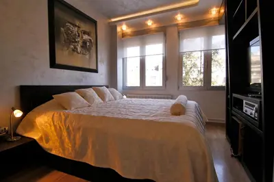 a bedroom with a bed with white sheets and windows at Business & Travel Apartments in Belgrade