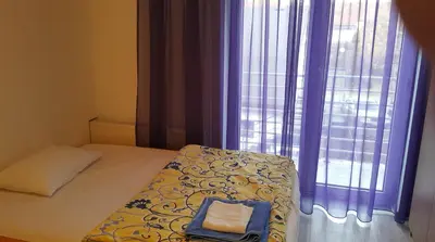 a bedroom with a bed and a window with purple curtains at Guest House Boska in Pančevo