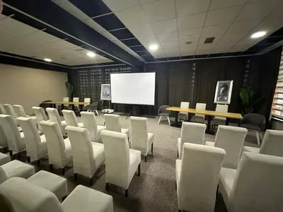 a conference room with white chairs and a white screen at Garnet Hotel & Event Centar in Ruma