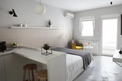 a white bedroom with a bed and a kitchen at Temple Apartments Belgrade in Belgrade