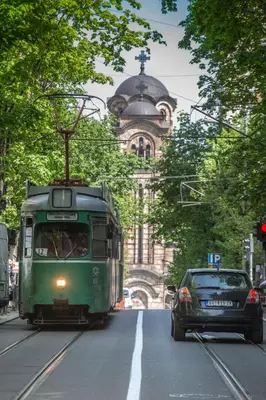 a green tram driving down a city street with a car at Cosmopolitan One Apartment in Belgrade