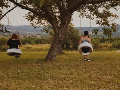 two women are sitting on swings under a tree at Branch in Arandjelovac