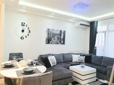 a living room with a couch and a table and a clock at Belgrade Waterfront-Delux apartman Beograd na vodi in Belgrade