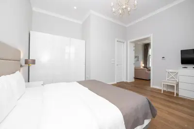 a white bedroom with a large bed and a television at Slavija Fontana Lux Apartments in Belgrade