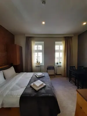 a bedroom with a bed with a table and two windows at Urban Lodge Belgrade in Belgrade