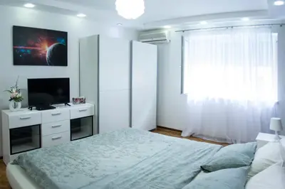 a white bedroom with a bed and a television at White Night City Center Apartman in Belgrade