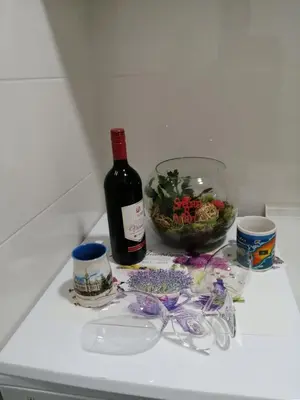 a bottle of wine and a bowl of flowers on a counter at Apartman Lux in Nova Pazova