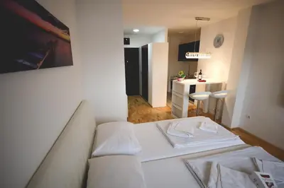 a living room with a white couch and a kitchen at Apartman Lux in Nova Pazova