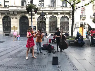 a woman in a red dress playingviolin on a city street at INNA Luxe & Wine- Central Belgrade Apartments in Belgrade