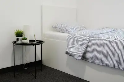 a white bedroom with a bed and a side table at St.Sava apartment in Belgrade