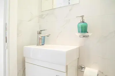 a white bathroom with a sink and a blue vase at Etoile City Center Apartments- Obilicev venac in Belgrade