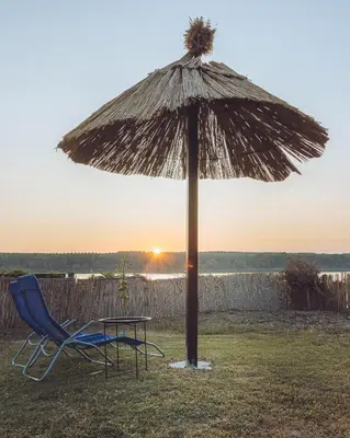 a table and a chair under a straw umbrella at Prenociste Dunav 97 K6 in Novi Banovci