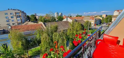 a balcony with red flowers and a view of a city at Julija in Pančevo