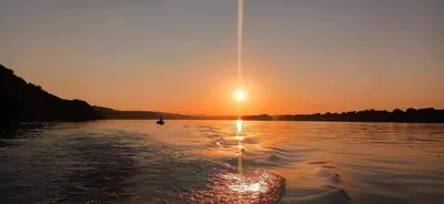 a boat on a lake with the sun setting at San na vodi in Smederevo