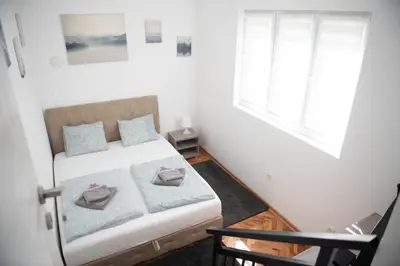a small bedroom with a bed and two windows at APARTMAN TEA 2 in Belgrade