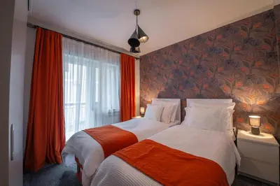 two beds in a bedroom with red curtains and a window at Apartmani Maximilian in Čukarica
