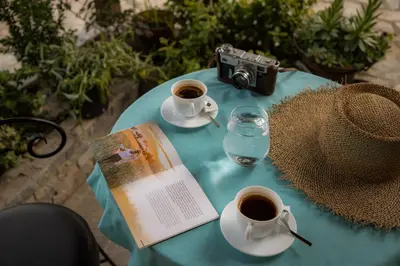 a table with a book and cups of coffee and a camera at Vila Lio & Restaurant Devojacki Bunar in Novi Vladimirovac