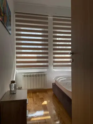 a bedroom with a bed and a window with blinds at Apartman Ambasador in Pančevo