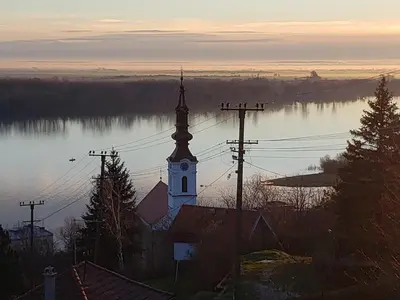 a church with a clock tower next to a body of water at Vila Slankamenka in Stari Slankamen